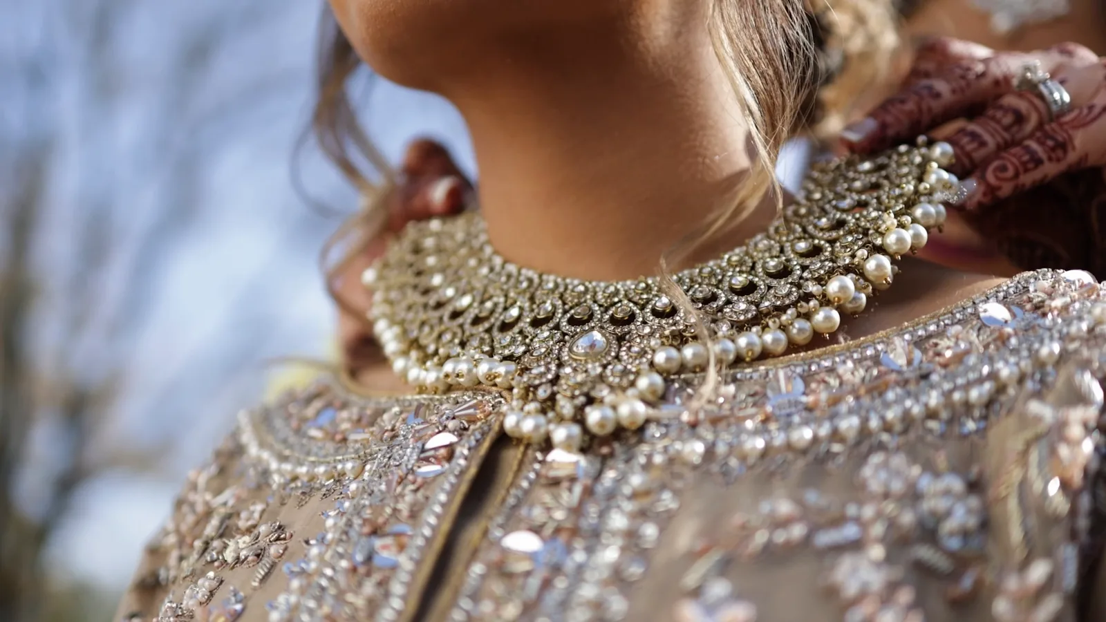 Close up of a bride wearing an ornate gold and pearl bridal necklace