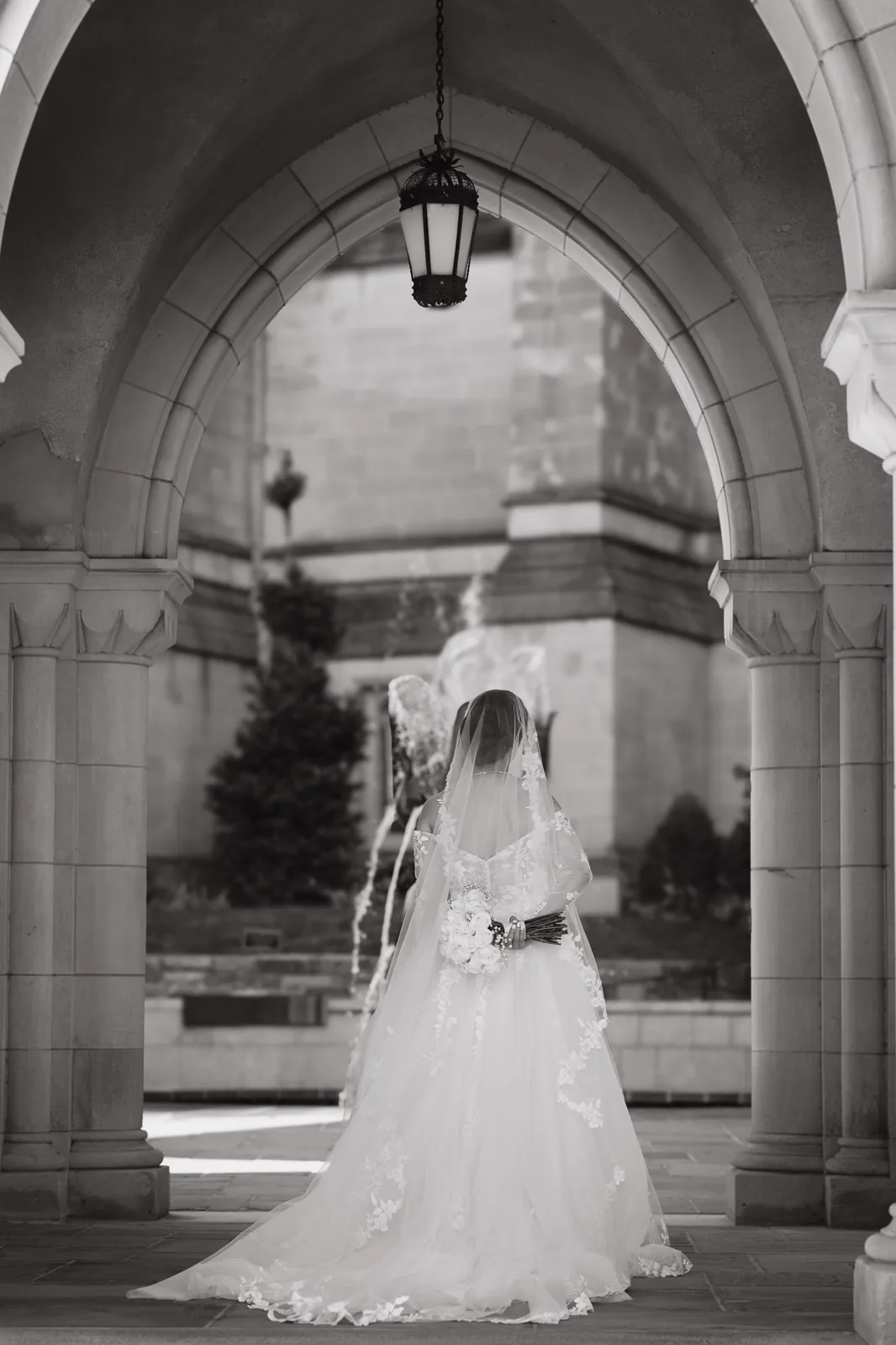 Black and white photo of a bride standing in a gothic stone archway