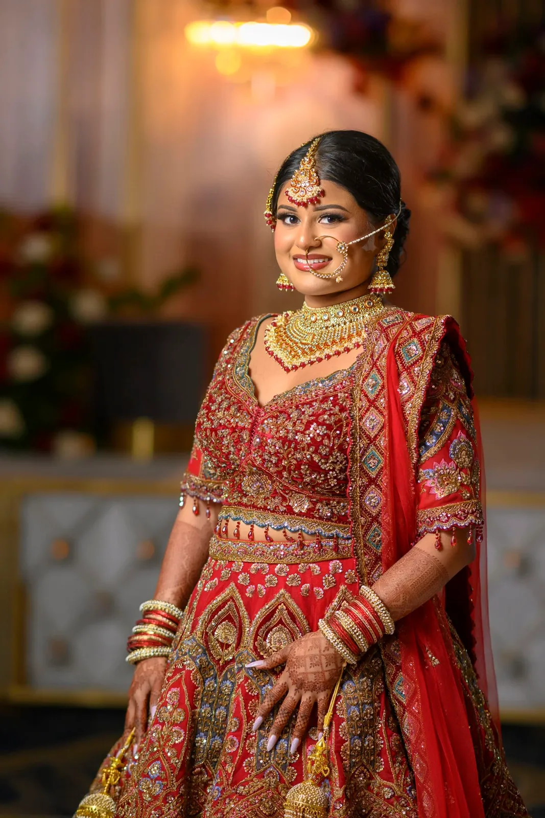 Indian bride in a red and gold lehenga standing in an elegant ballroom